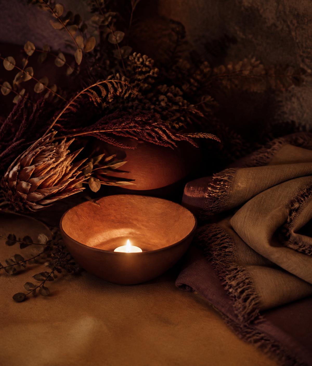 Candlelit clay bowl, dried botanicals and folded linen